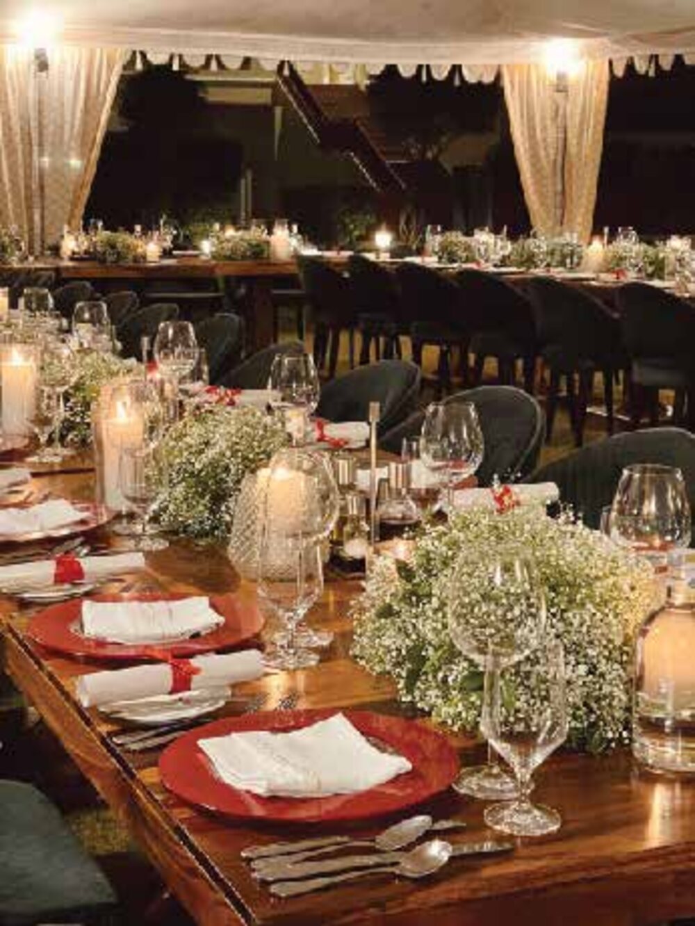 A long candlelit dinner table styled with baby's breath and red accents