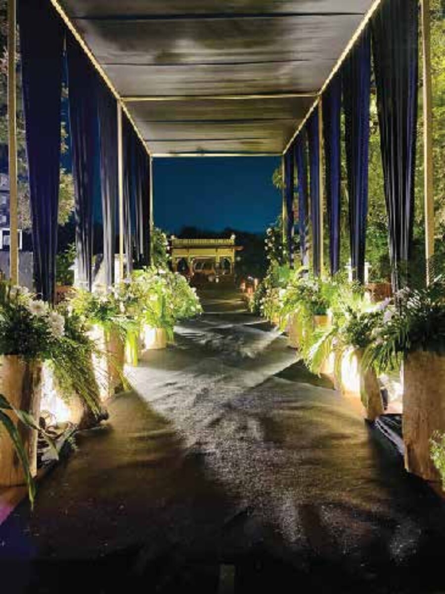 A draped walkway lined with lit florals leading to a golden pavilion at night