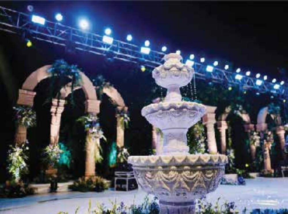 A stone fountain beneath a lit colonnade of arches at a garden wedding venue