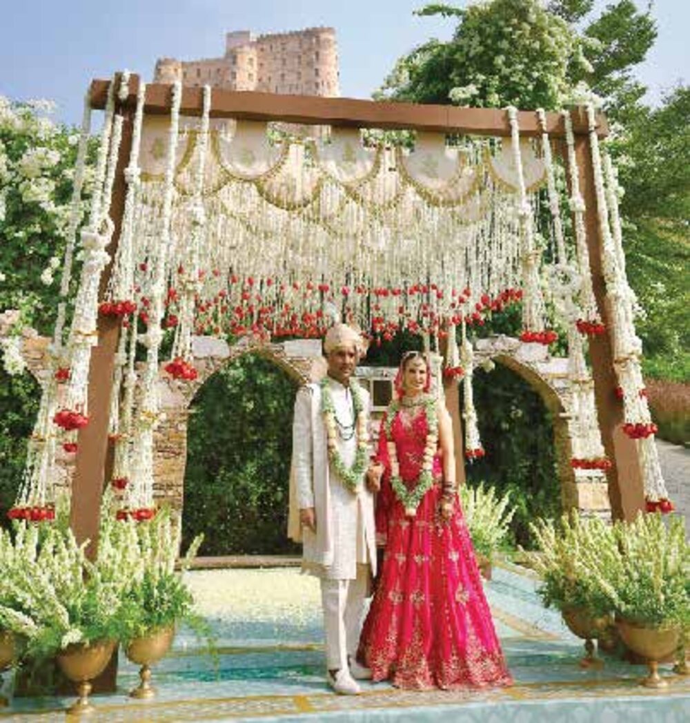 A bride and groom beneath a jasmine and rose mandap with a fort in the background